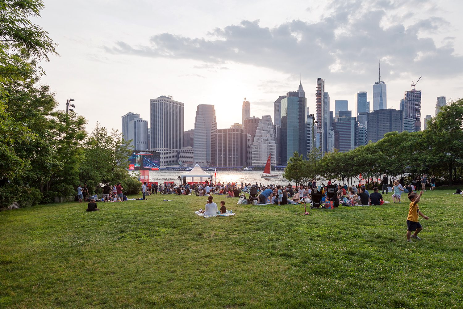 A crowd on the Harbor View Lawn at Brooklyn Bridge Park's Pier 1 with the Manhattan skyline behind
