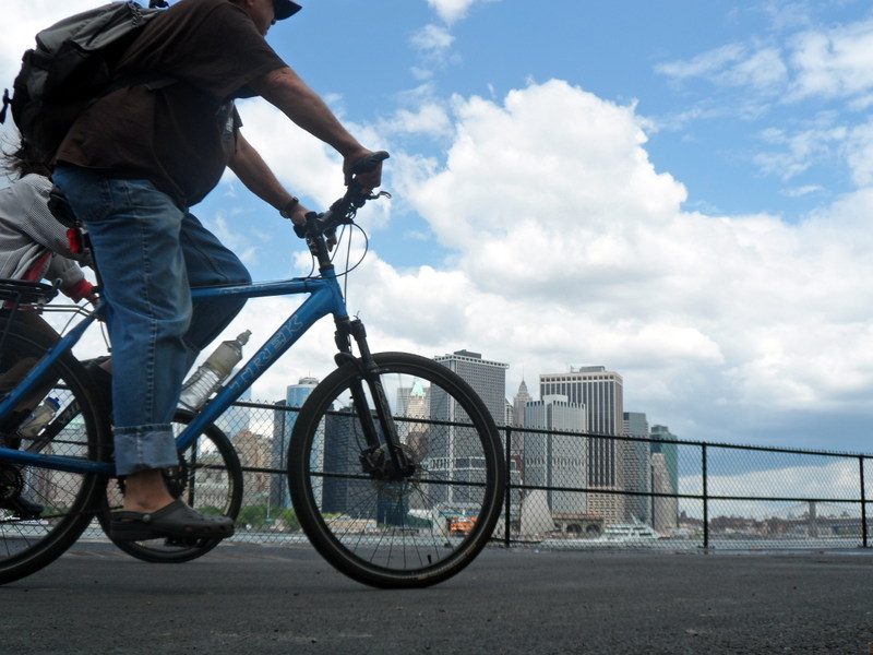 Families biking the car-free paths on Governors Island with the Manhattan skyline behind