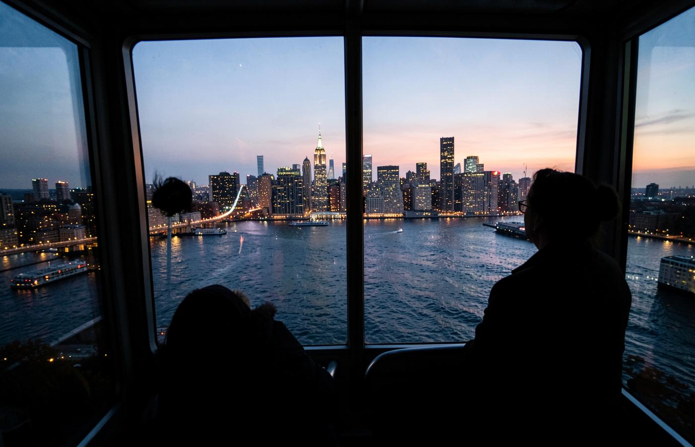 View of the lit Midtown Manhattan skyline at dusk from inside the Roosevelt Island aerial tram on an autumn evening